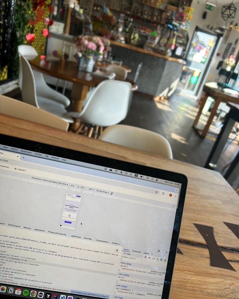 A laptop on a café table showing browser developer tools open in responsive-design mode while building a site
